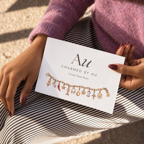 Charmed by AU gift card front, held in sunlight, showing the illustrated charm bracelet